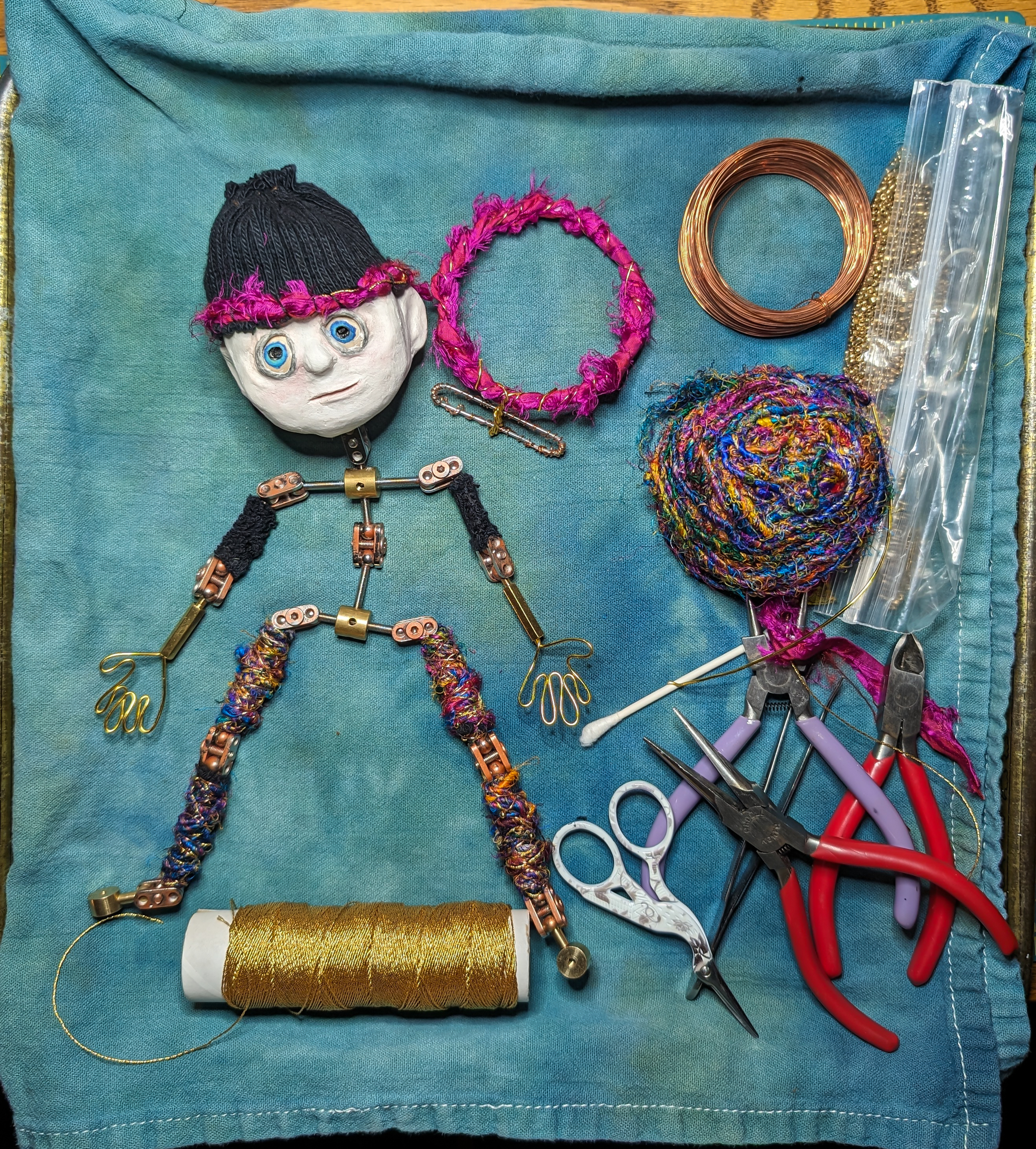 Doll being wrapped boho style with silk yarn, gold thread, gold beads, and copper wire